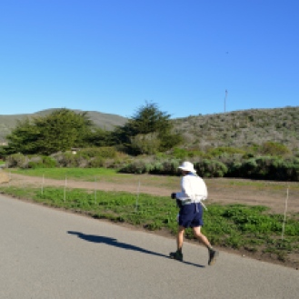 A jogger keeps a steady pace, breathing heavily as he pushes himself to keep running despite the wind and heat.